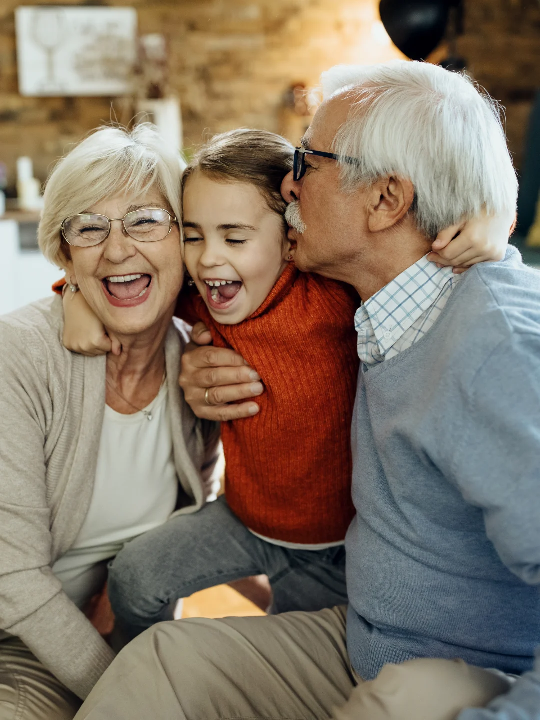 Unos abuelos ríen abrazados con su nieta en casa